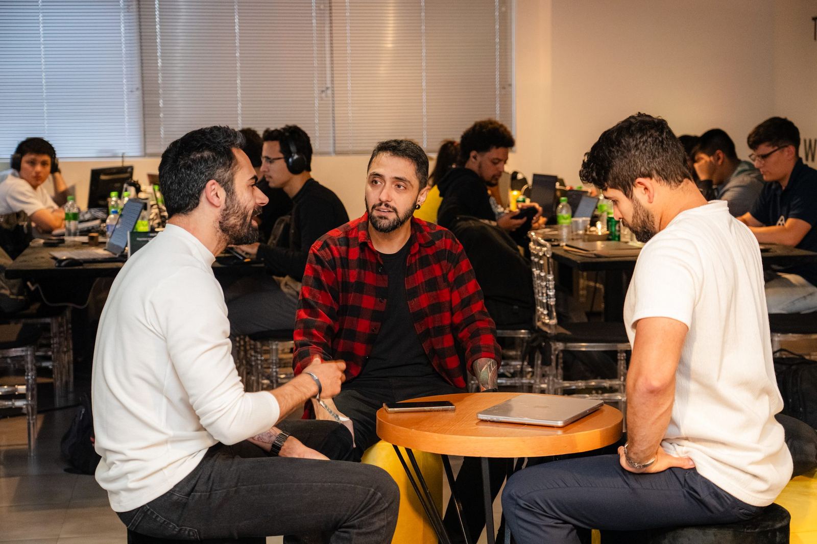 Three participants talking around a small table in the coworking space, with other teams working in the background.